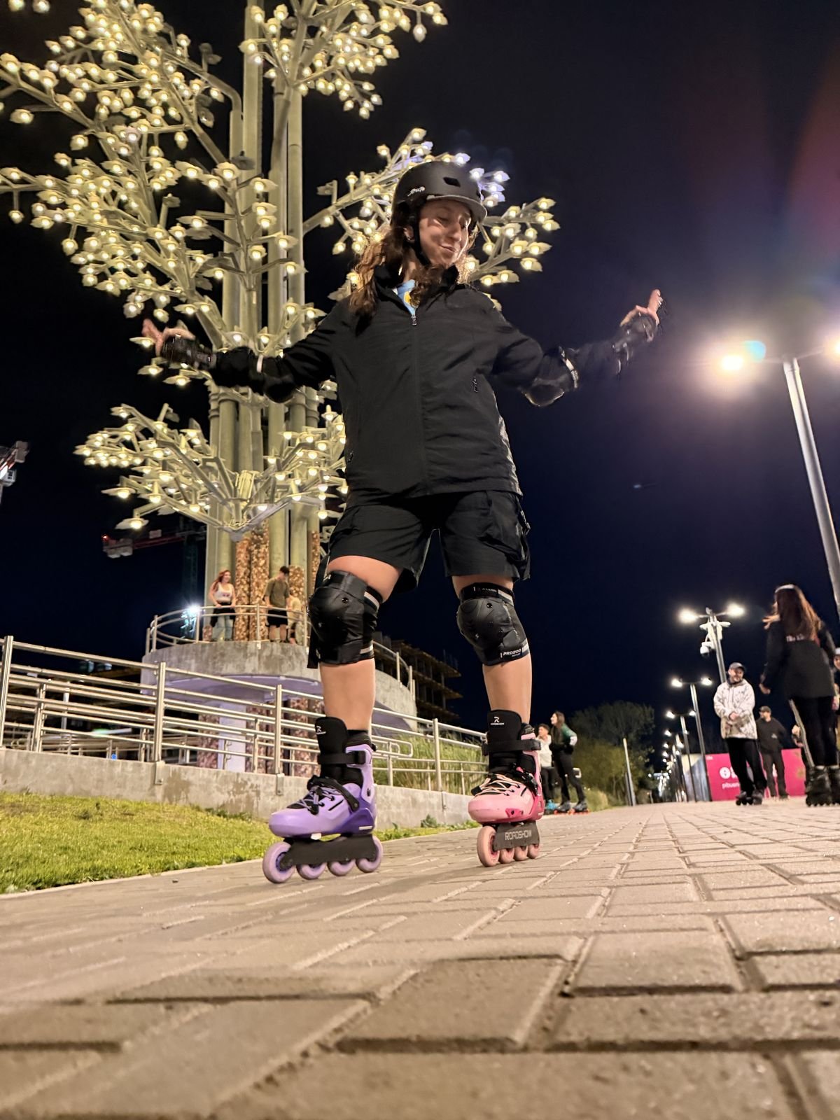 Patinadora con los brazos abiertos junto a un árbol iluminado